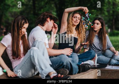 Students studying together outdoors examining a molecular model with a laptop in the park Stock Photo