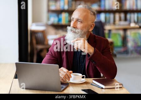 Thoughtful senior man sitting at cafe, using laptop Stock Photo