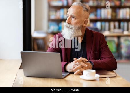 Pensive grey-haired businessman using laptop at cafe, looking through window Stock Photo