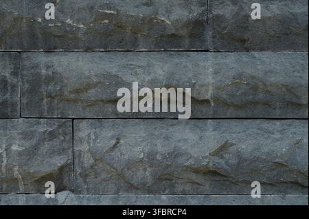 A detailed close up of stacked split face travertine wall stone. The natural stone tiles have a rough, chiseled front surface with a layered, linear a Stock Photo