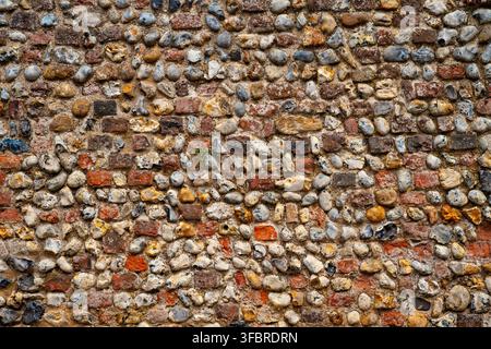Close-up of a traditional flint and brick wall facade in Lavenham, Suffolk, England. Mixed stone and brick texture with weathering and a small plant g Stock Photo