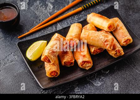Fried spring rolls served with sauce and lime on a black plate Stock Photo