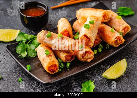 Fried spring rolls served with sauce and lime on a black plate Stock Photo