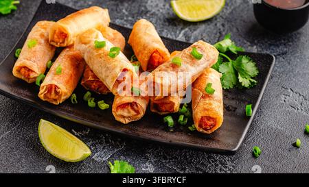 Fried spring rolls served with sauce and lime on a black plate Stock Photo