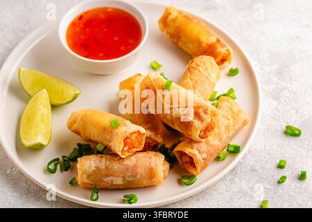 Fried spring rolls served with lime and sauce on a white plate Stock Photo