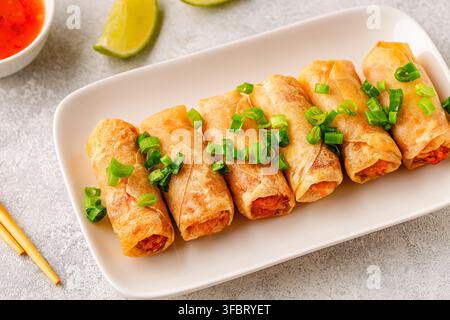 Fried spring rolls served with lime and sauce on a white plate Stock Photo