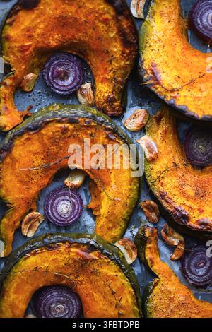 Top view of roasted pumpkin wedges with red onion rings and herbs on baking tray. Autumn comfort food with squash and rustic homemade cooking Stock Photo