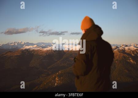Person overlooking mountain ranges illuminated by sunset light in the Dolomites. Scenic alpine landscape with layered ridges and autumn colors Stock Photo