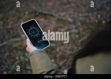 Woman using a digital compass on smartphone for navigation and finding direction while exploring a forest Stock Photo