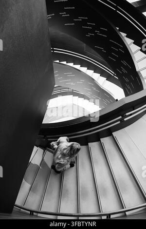 Helsinki, Finland - February 28th 2026: Person descends spiral staircase beneath Finnish text in modern public interior. Stock Photo