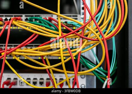 Messy tangle of vibrant yellow, red, and green Ethernet patch cables routed across network switches and patch panels inside a server rack Stock Photo