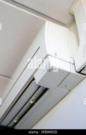 Standard wall-mounted indoor split-system air conditioner unit installed on an interior wall, featuring a compact white housing, air outlet grille Stock Photo