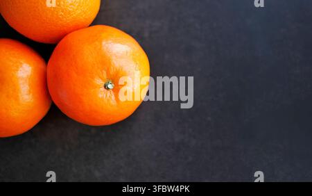 High angle view of ripe organic tangerines. Vibrant orange fruit on black  texture. Minimalist composition perfect for food marketing, health banners, Stock Photo