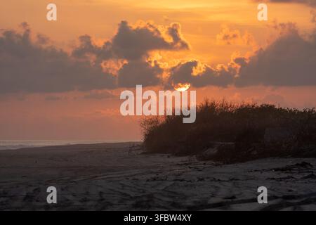 Sunset illuminating clouds over a quiet beach with sand and sparse vegetation Stock Photo