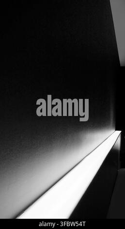 Dramatic architectural background featuring a dark textured wall illuminated by a white LED light strip. The diagonal lighting creates a glowing gradi Stock Photo
