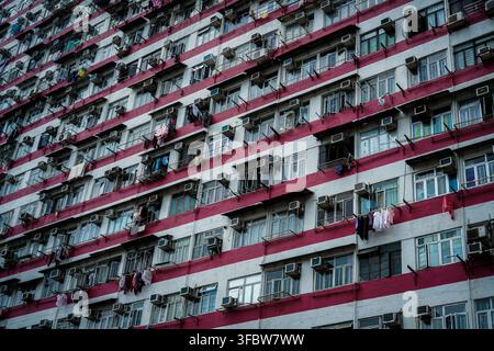The exterior of a high-rise residential apartment building in Hong Kong features alternating horizontal red and white painted stripes, with numerous w Stock Photo