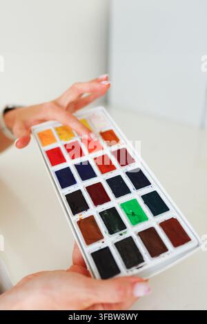 Close-up of hands holding a colorful watercolor paint palette, creative art supplies for painting and artistic hobbies. Stock Photo