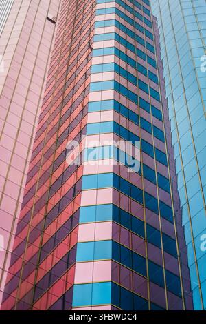A detailed view focuses on the corner of a modern skyscraper featuring alternating pink and light blue glass panels, with an adjacent building reflect Stock Photo