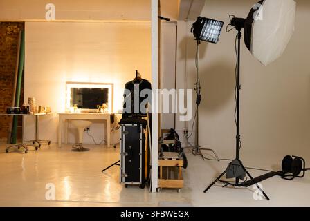 Lighting setup is standing on right side of studio with softbox, LED panel, cables. Makeup, vanity, mirror, wardrobe, backdrop, brick, partition Stock Photo