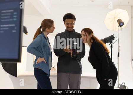 Diverse creative team reviewing DSLR camera with external flash on monitor in white studio. Photography, lighting, backdrop, softbox, strobe, collabor Stock Photo