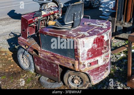 An old, worn-out maroon industrial forklift parked outside on gravel. Stock Photo