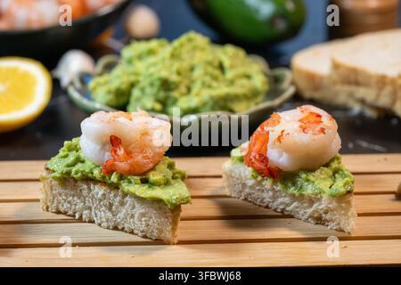 delicious canapes topped with guacamole and shrimp, arranged on a wooden board Stock Photo