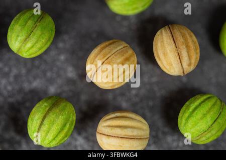 A flat-lay shot of traditional walnut-shaped cookies  in green and natural golden colors scattered on a dark textured surface. Stock Photo