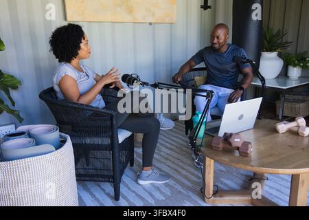 African American colleagues sitting in studio using microphones and laptop, woman in activewear Stock Photo