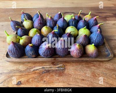 Angled front view of ripe purple and green figs arranged on a wooden tray over a rustic wooden table. Concept for organic harvest, fresh fruits Stock Photo