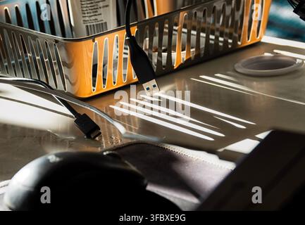 A desk setup featuring an orange plastic storage basket, a black computer mouse, and various USB cables Stock Photo