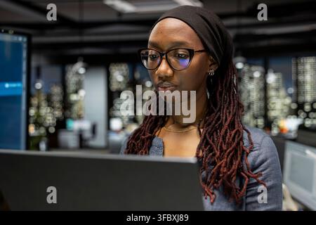 Technician using laptop in startup office, optimizing code for performance and scalability, doing quality assurance. African american woman looking at programming language on device Stock Photo