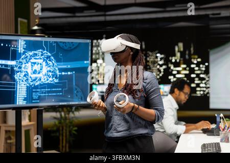 Woman using virtual reality in tech startup office to develop programs using AI automation. IT specialist wearing VR headset gear, debugging applications with artificial intelligence Stock Photo