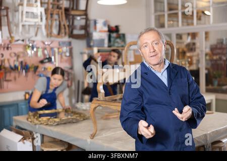 Professional elderly craftsman restorer in uniform looking at camera while working in repair shop Stock Photo