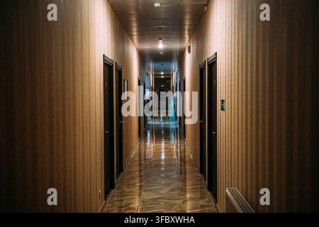 Empty corridor hallway interior architecture hospitality property concept, with closed doors, reflective floor, warm lighting and deep perspective in quiet building. Stock Photo