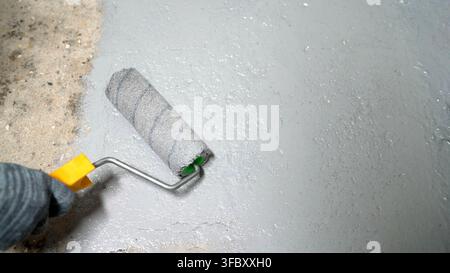 Construction worker applying epoxy resin with paint roller on concrete floor for waterproofing Stock Photo