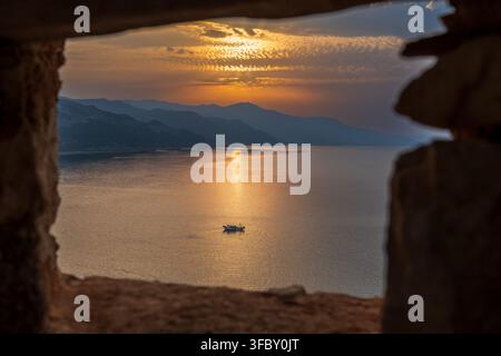 Dramatic golden sunset over the Mediterranean Sea framed through a rustic stone window opening in El Jebha, northern Morocco. Stock Photo