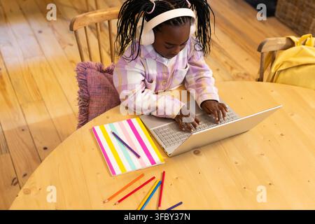 African American child female typing on silver laptop at home study table with white headphones Stock Photo