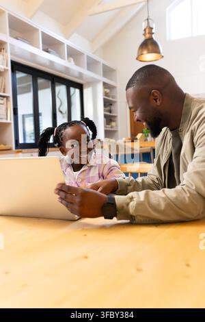Father in khaki jacket with daughter child sitting at large wooden table using laptop in kitchen Stock Photo