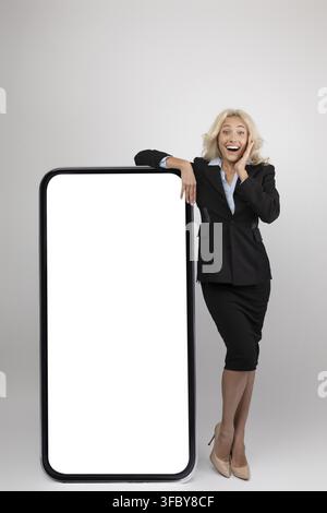 Smiling Young Caucasian Businesswoman Presenting Blank Smartphone Screen, Corporate Office Setting Stock Photo