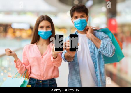 Happy Young Couple Using Smartphones While Shopping In Mall, Retail Experience Stock Photo
