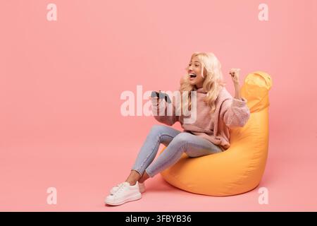 Excited Young Woman Playing Video Games On Sofa With Joystick, Pink Background Stock Photo