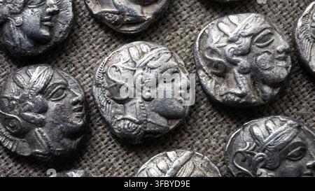 Close-up of coins of ancient Athens with profile faces on rustic textile. Top view of old silver tetradrachms, flat lay of antique Greek money, classi Stock Photo