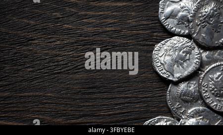 A top-down, flat lay photograph featuring a cluster of ancient silver coins resting on a dark, heavily textured rustic wooden surface. The coins, posi Stock Photo