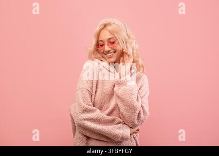 Smiling Young Woman In Cozy Pink Sweater With Sunglasses Posing In Front Of Pink Background Stock Photo