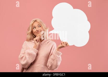 Thoughtful Young Woman Holding Blank Speech Bubble, Pink Background, Casual Portrait Stock Photo