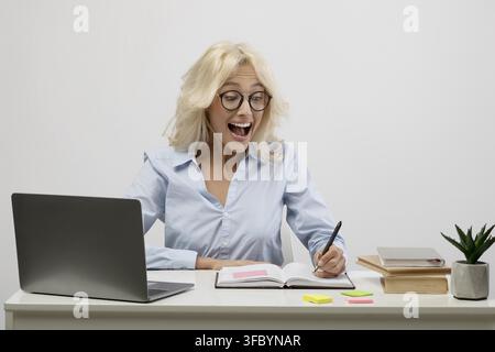 Excited Young Caucasian Woman Writing Notes At Desk In Office, Business Concept Stock Photo