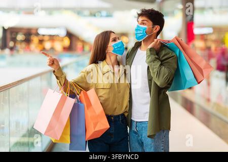 Young Couple Shopping Together In Mall, Wearing Face Masks, Happy And Excited Stock Photo