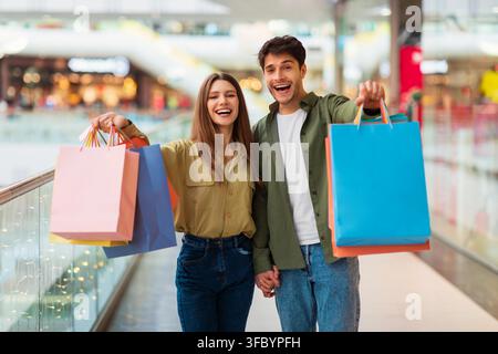 Happy Young Couple Holding Colorful Shopping Bags In Shopping Mall, Shopping Concept Stock Photo