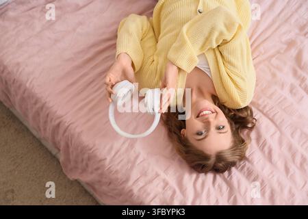 Relaxation and leisure time, young woman enjoying music with headphones while lying on a pink bed at home Stock Photo