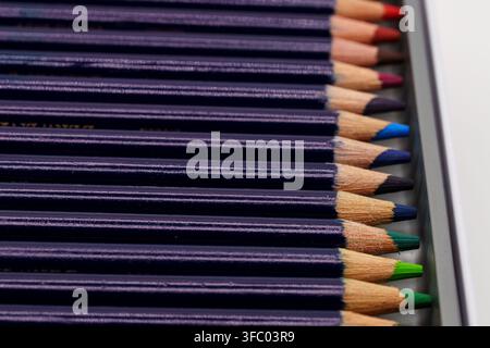 A neatly organized set of professional colored pencils displayed in a metal storage tin, showing sharpened tips in a rainbow spectrum of colors. The c Stock Photo